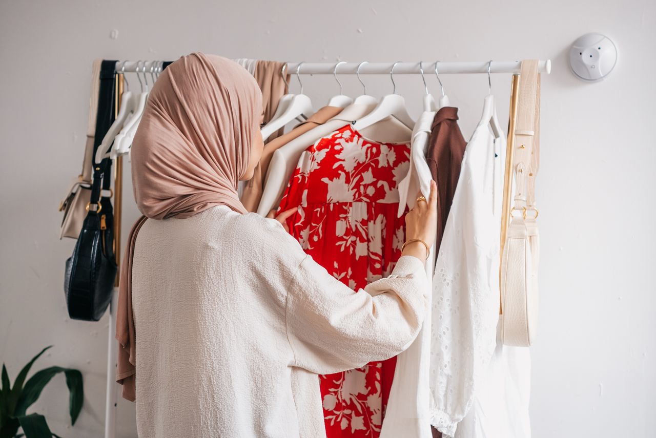 Crafting Captivating Headlines: Your awesome post title goes here Woman in hijab organizing wardrobe, selecting various clothing options indoors.