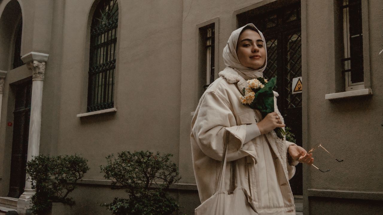 Young woman in hijab holding flowers on a historic street in Istanbul.